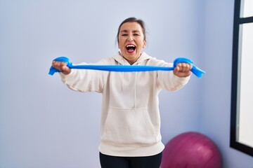 Middle age hispanic woman training arm resistance with elastic arm bands smiling and laughing hard out loud because funny crazy joke.