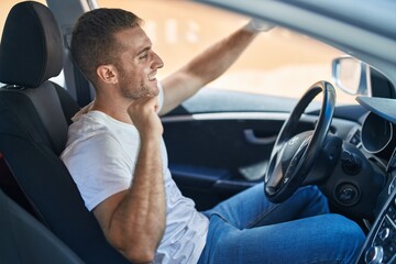 Young caucasian man sitting on car dancing at street