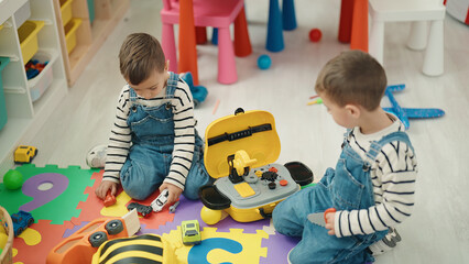 Adorable boys sitting on floor playing with car toys at kindergarten