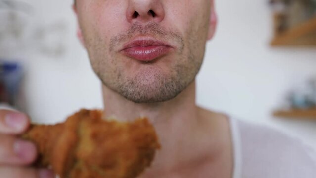 Hungry excited guy eating fried chicken wings. Caucasian man enjoying junk food. high calorie food, health risks, cholesterol. Close up of male mouth eating junk food indoors. 