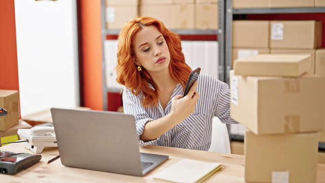 Young redhead woman ecommerce business worker scanning packages using smartphone at office