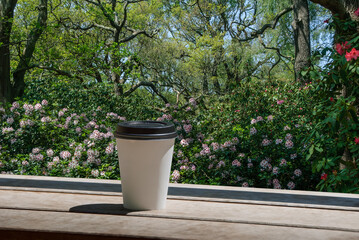 Unbranded, disposable coffee cup mock up with Rhododendron flowers in the background. Cup of coffee...