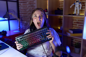 Young caucasian woman holding gamer keyboard angry and mad screaming frustrated and furious, shouting with anger looking up.