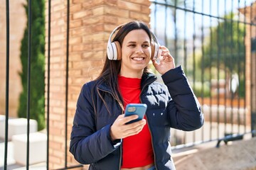 Young beautiful hispanic woman smiling confident listening to music at street