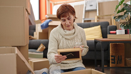 Mature hispanic woman unpacking cardboard box drinking wine at new home