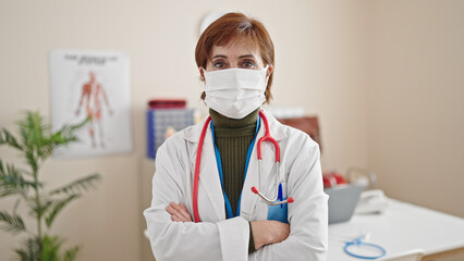 Fototapeta na wymiar Mature hispanic woman doctor standing wearing medical mask at clinic
