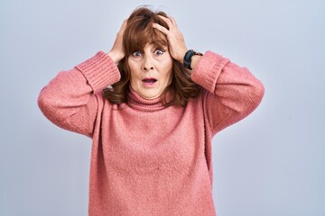 Middle age hispanic woman standing over isolated background crazy and scared with hands on head, afraid and surprised of shock with open mouth