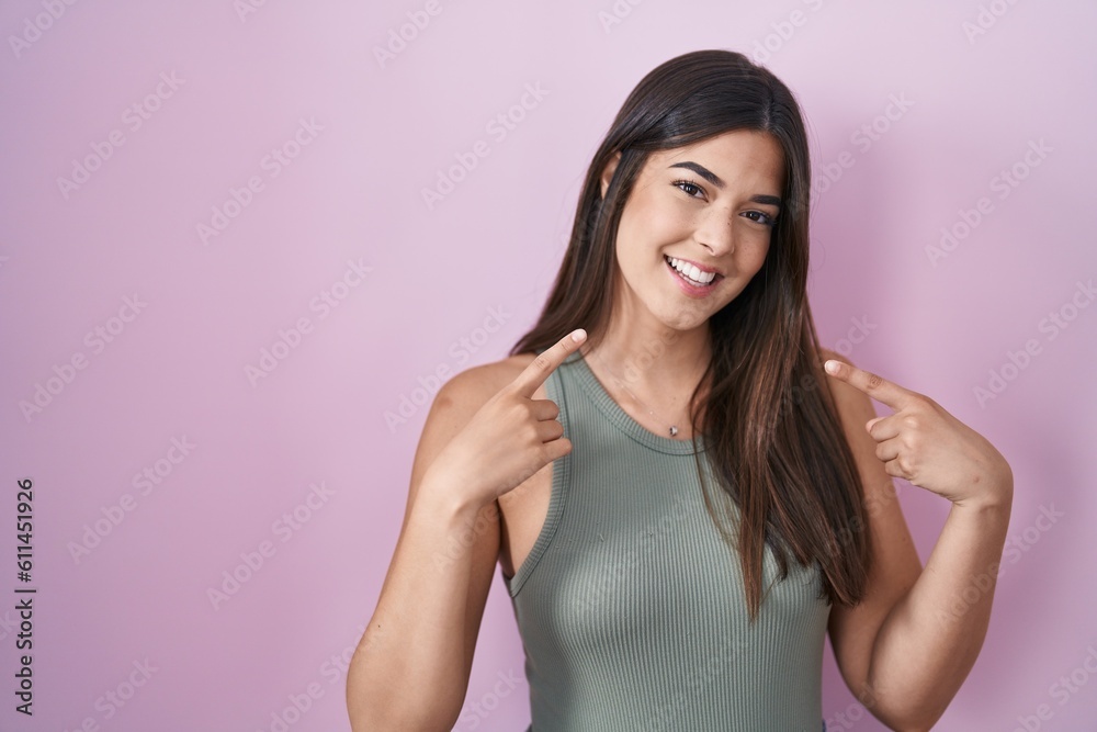 Poster Hispanic woman standing over pink background smiling cheerful showing and pointing with fingers teeth and mouth. dental health concept.