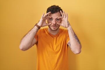 Fototapeta na wymiar Young hispanic man standing over yellow background trying to open eyes with fingers, sleepy and tired for morning fatigue