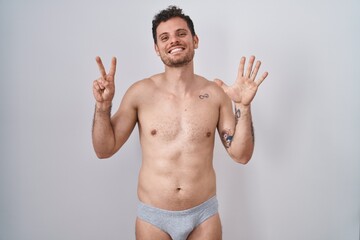 Fototapeta premium Young hispanic man standing shirtless wearing underware showing and pointing up with fingers number seven while smiling confident and happy.