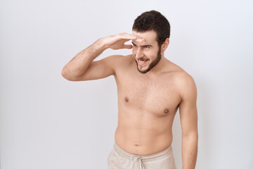 Fototapeta premium Young hispanic man standing shirtless over white background very happy and smiling looking far away with hand over head. searching concept.