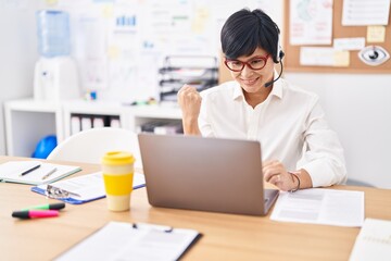 Young asian woman with short hair wearing call center agent headset screaming proud, celebrating victory and success very excited with raised arm
