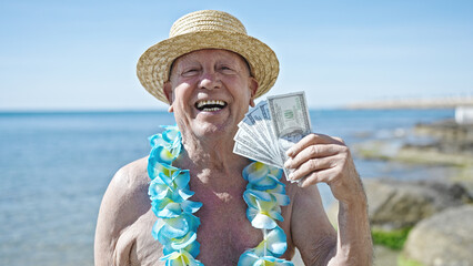 Senior grey-haired man tourist wearing swimsuit and summer hat holding dollars at seaside