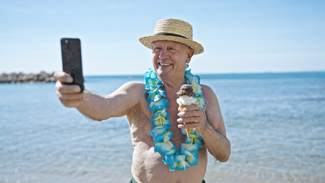 Senior grey-haired man tourist holding ice cream make selfie by smartphone at seaside