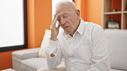 Fototapeta premium Senior grey-haired man worried with hand on forehead at home