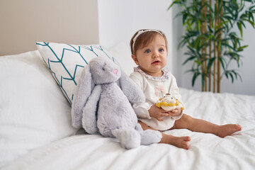 Adorable caucasian baby sitting on bed playing with doll at bedroom