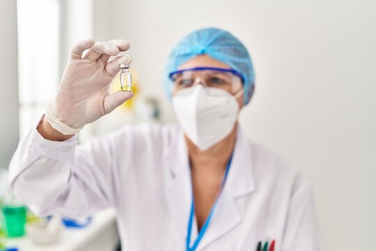Middle age woman wearing scientist unifor and medical mask holding dose vaccine at laboratory