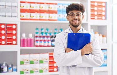 Young arab man pharmacist smiling confident hugging clipboard at pharmacy