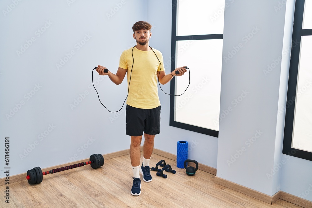 Wall mural Arab man with beard training with jump rope puffing cheeks with funny face. mouth inflated with air, catching air.