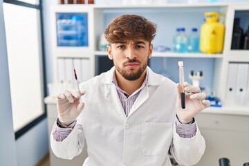 Arab man with beard working at scientist laboratory holding blood sample skeptic and nervous, frowning upset because of problem. negative person.