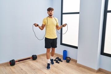 Arab man with beard training with jump rope puffing cheeks with funny face. mouth inflated with...