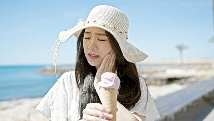 Young chinese woman tourist eating ice cream suffering teeth pain at seaside