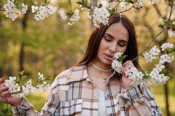 A girl in a plaid is standing near a flowering tree. Portrait of a beautiful young woman