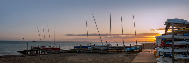 Fototapeta na wymiar SOUTHEND-ON-SEA, ESSEX, UK - SEPTEMBER 10, 2009: Panorama view of dinghies and sailboards on a jetty at Thorpe Esplanade with a setting sun and Southend Pier in the background