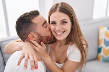 Man and woman couple sitting on sofa kissing at home