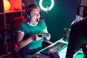 Young redhead woman streamer playing video game using joystick at gaming room