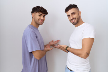 Homosexual gay couple standing over white background inviting to enter smiling natural with open hand