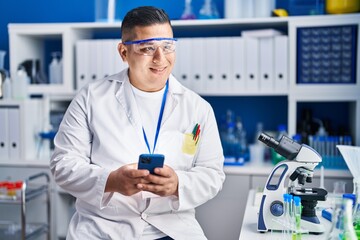 Young latin man scientist smiling confident using smartphone at laboratory