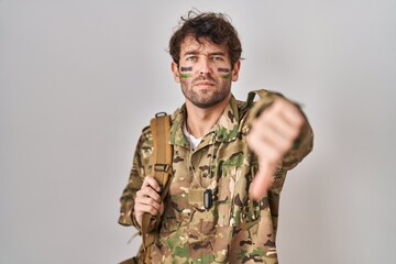 Hispanic young man wearing camouflage army uniform looking unhappy and angry showing rejection and negative with thumbs down gesture. bad expression.