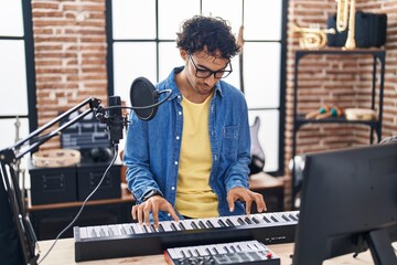 Young hispanic man musician playing piano keyboard at music studio