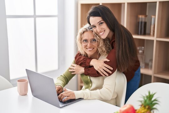 Two women mother and daughter hugging each other using laptop at home