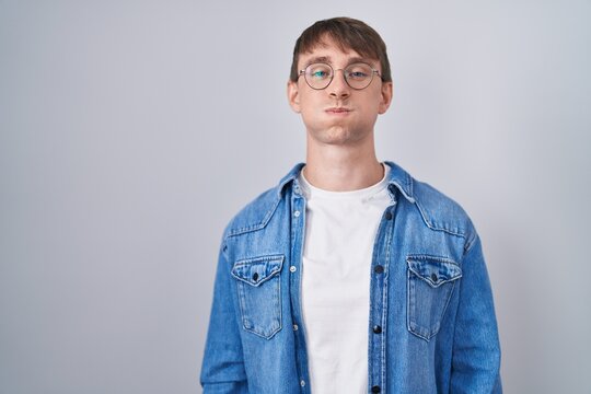 Caucasian blond man standing wearing glasses puffing cheeks with funny face. mouth inflated with air, crazy expression.