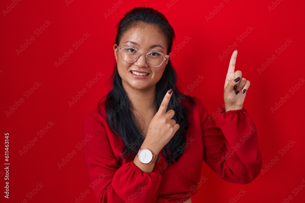 Poster Asian young woman standing over red background smiling and looking at the camera pointing with two hands and fingers to the side.