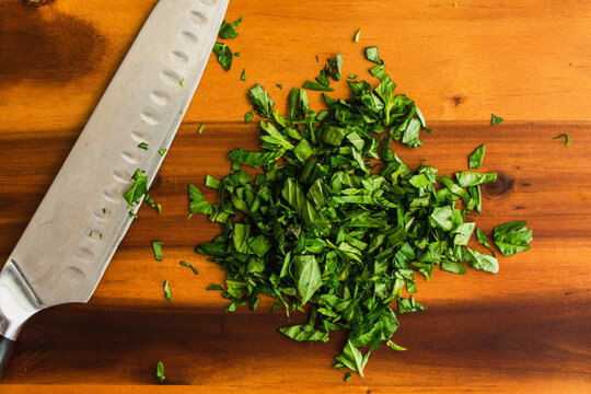 Chopped Basil with a Chef's Knife on a Wooden Cutting Board: Prepped Genovese basil leaves on a wood chopping board with a santoku knife