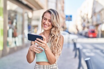 Young blonde woman smiling confident watching video on smartphone at street
