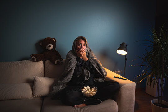 A girl home alone, spellbound by a horror film. Wide-eyed, she leans in, captivated by the flickering TV glow, engrossed in the terrifying narrative. Shadows amplify the suspense, making for an intens