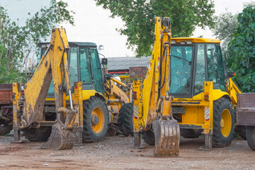 Yellow used excavators in a row stand in a parking lot after work.