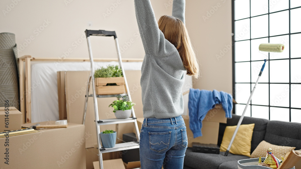 Poster young blonde woman standing with arms open at new home