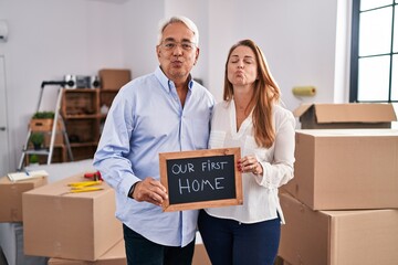 Middle age hispanic couple moving to a new home holding banner looking at the camera blowing a kiss being lovely and sexy. love expression.