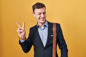 Caucasian business man over yellow background smiling with happy face winking at the camera doing...