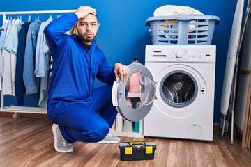 Hispanic repairman working on washing machine stressed and frustrated with hand on head, surprised and angry face