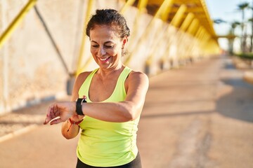 Middle age hispanic woman working out with smart watch at promenade