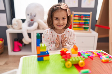 Adorable hispanic girl playing with construction blocks clapping hands at kindergarten