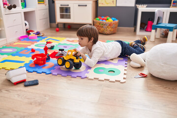 Adorable caucasian boy sitting on floor playing with tractor at kindergarten