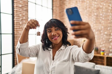 Young beautiful latin woman having video call holding key at new home