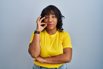 Hispanic woman standing over blue background mouth and lips shut as zip with fingers. secret and...